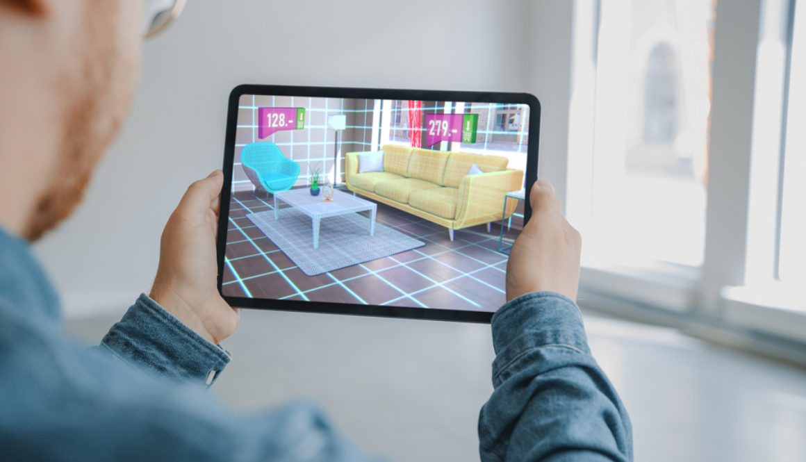 Shutterstock_1712828788 Decorating Apartment: Man Holding Digital Tablet with AR Interior Design Software Chooses 3D Furniture for Home from Online Shop with Shown Prices. Over Shoulder Screen Shot with 3D Render